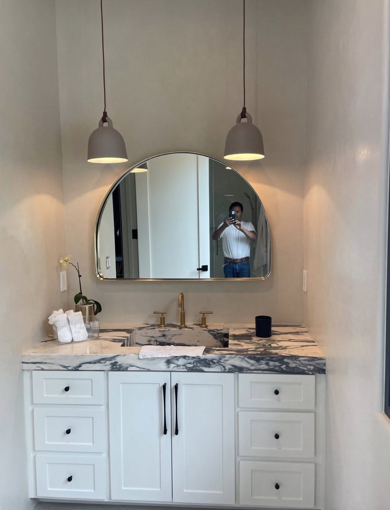 Vanity with marble top, brass faucet, pendant lights, and an arched mirror