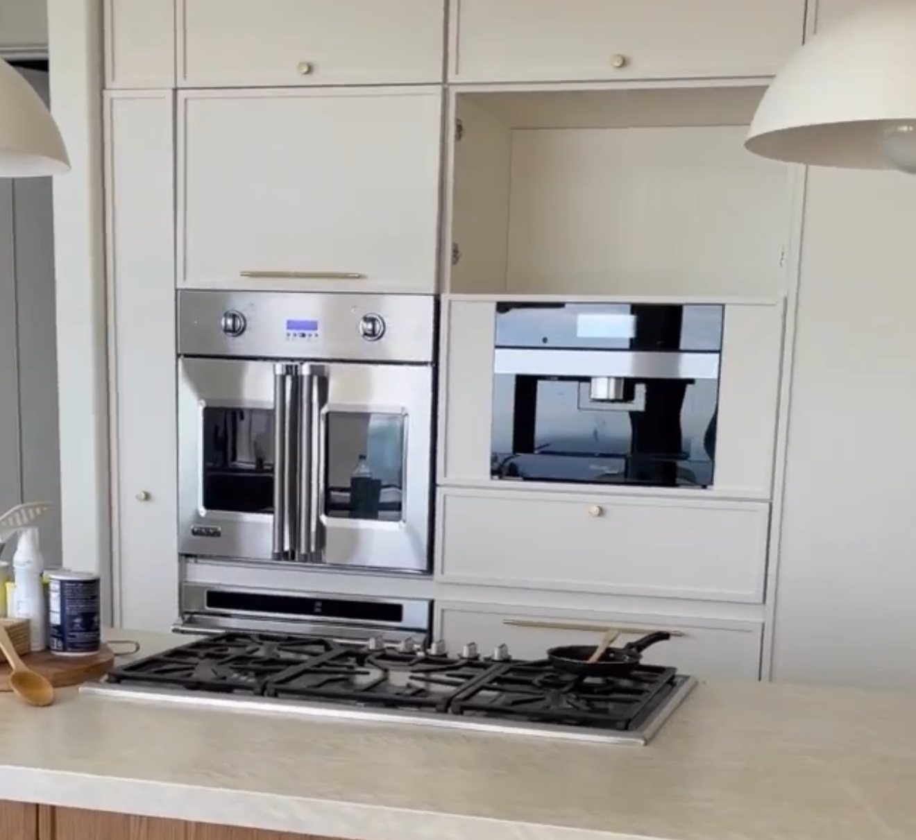 Paneled wall of built-in ovens behind an oak island with a gas cooktop