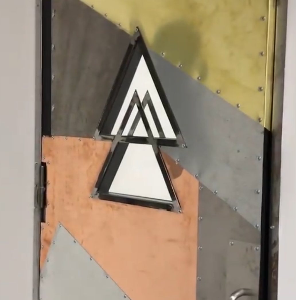 Custom riveted copper, brass, and steel door with a triangle window at Ad Astra School