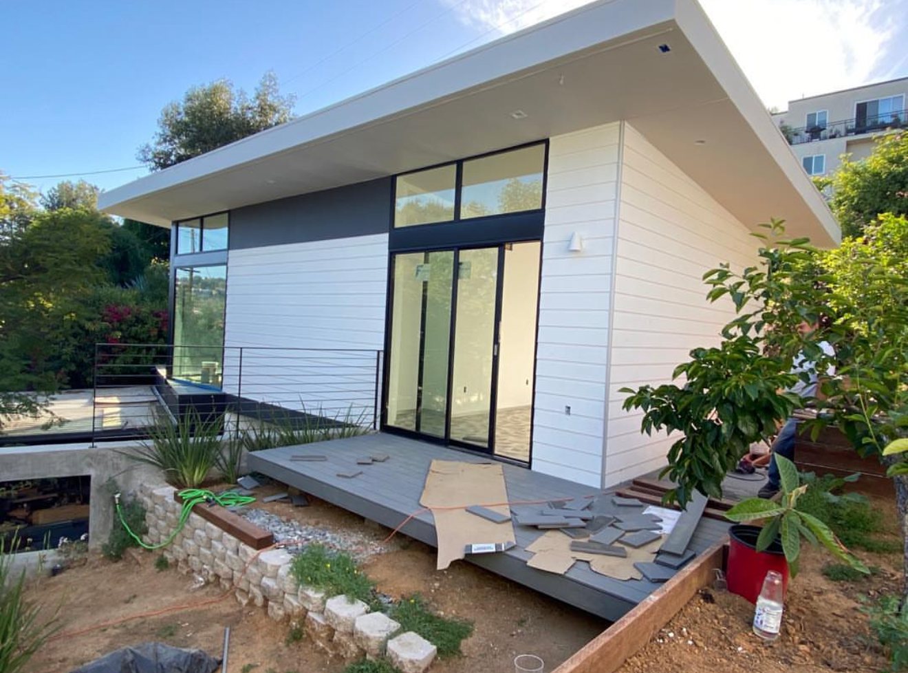 Modern studio with white lap siding, black-framed glass doors, and a new deck