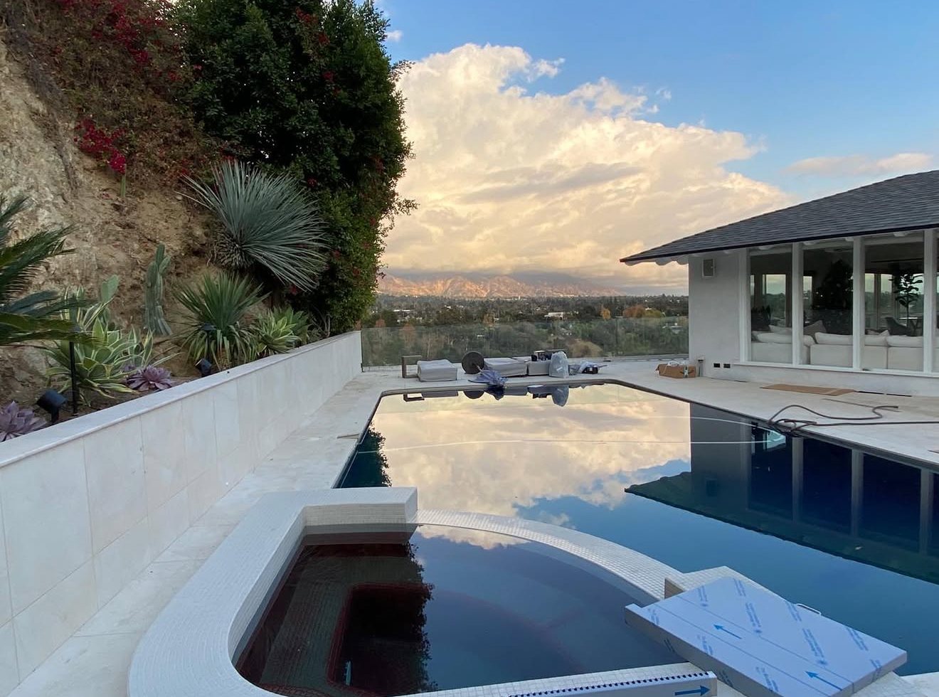 Pool and spa beside a planted hillside retaining wall at sunset