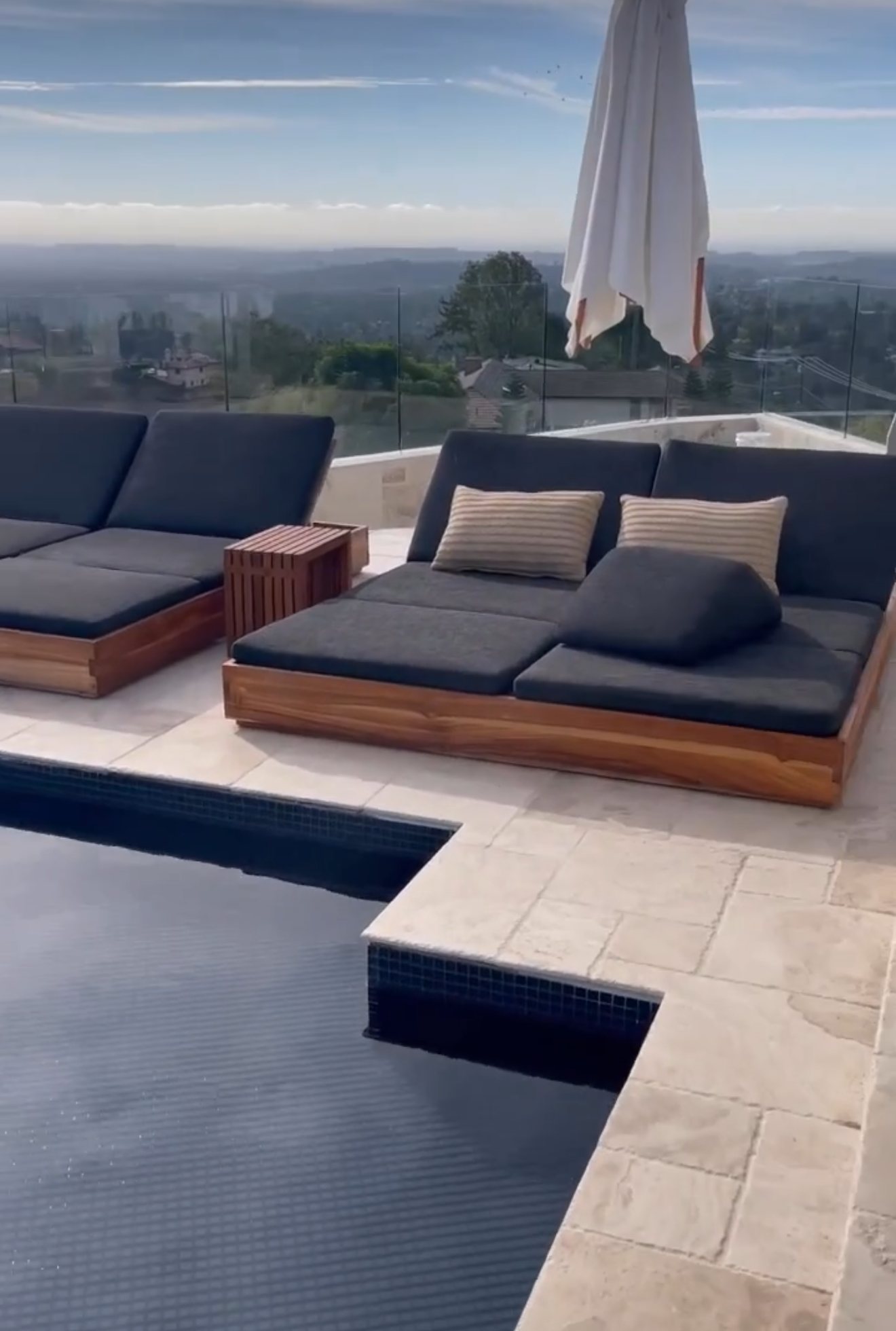 Rooftop pool with travertine deck, teak loungers, and glass railing