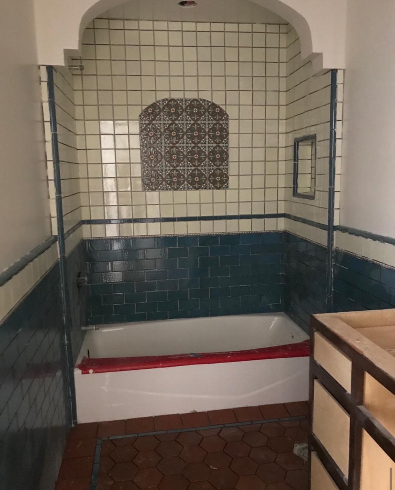 Arched tub alcove with cream and teal tile and an arched Talavera panel