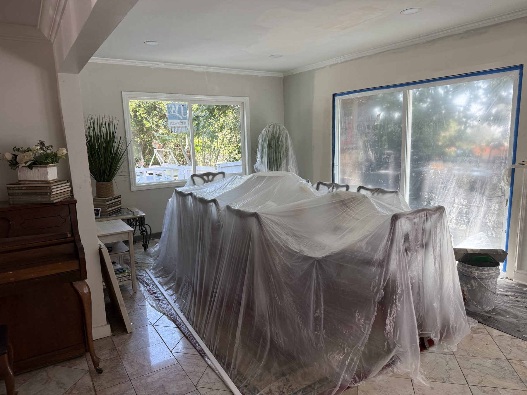 Living room with furniture wrapped in plastic and windows taped while walls are repaired