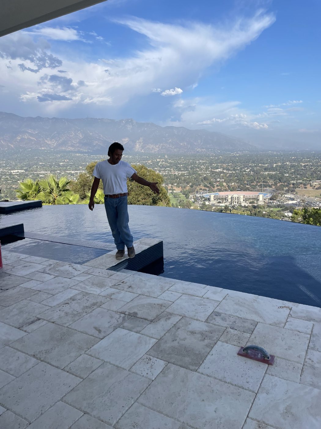 Humberto walking the edge of a finished infinity pool above Pasadena, with the Rose Bowl and the San Gabriel Mountains behind him